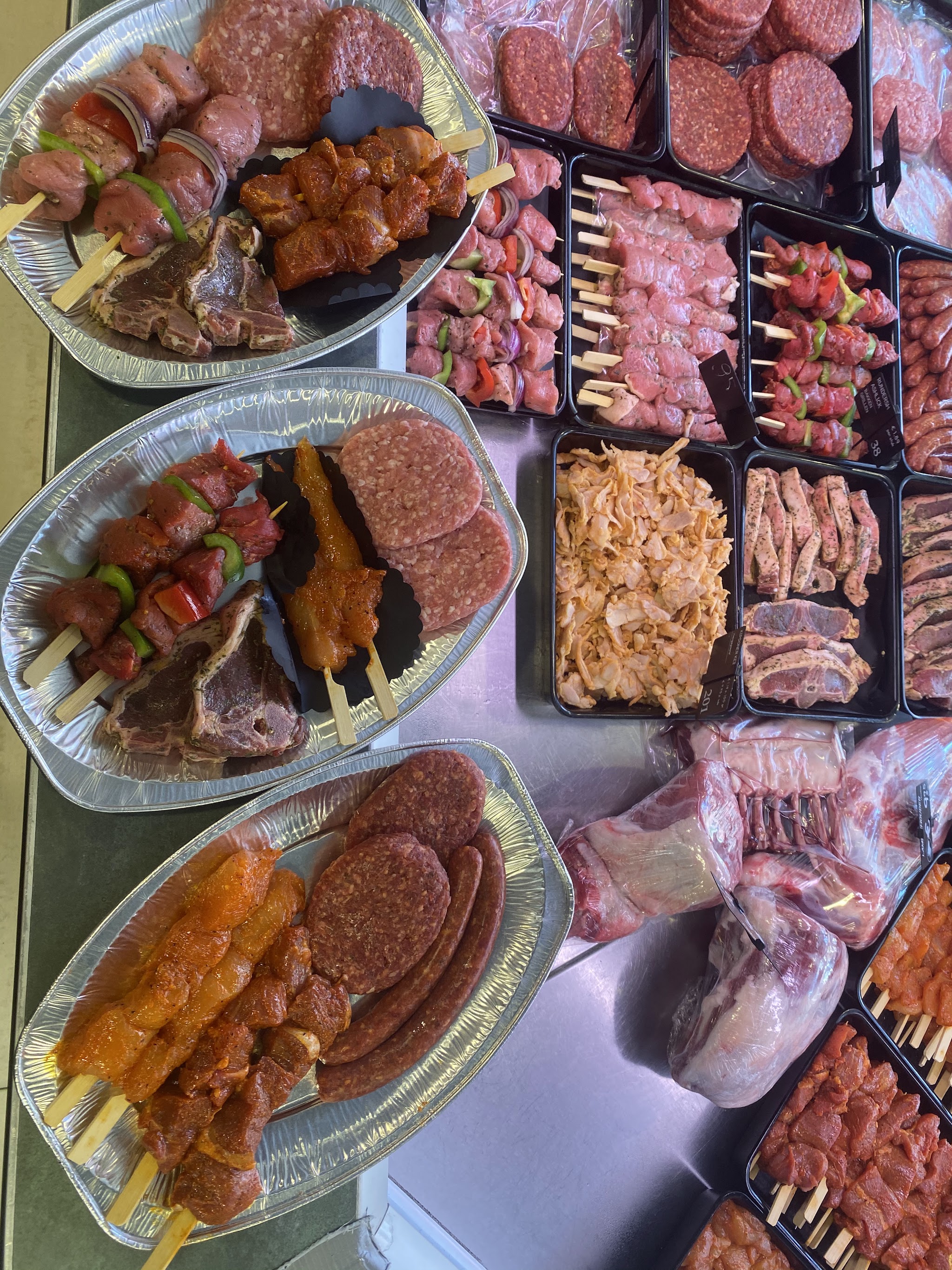 BBQ-schalen met spiesen, hamburgers en lamskoteletten naast de gevulde toonbank